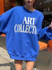 Person wearing a blue sweatshirt with 'ART COLLECTION' text outdoors.