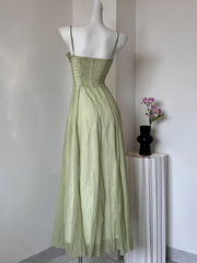 Green dress on a mannequin against a plain wall with a small plant in the background.