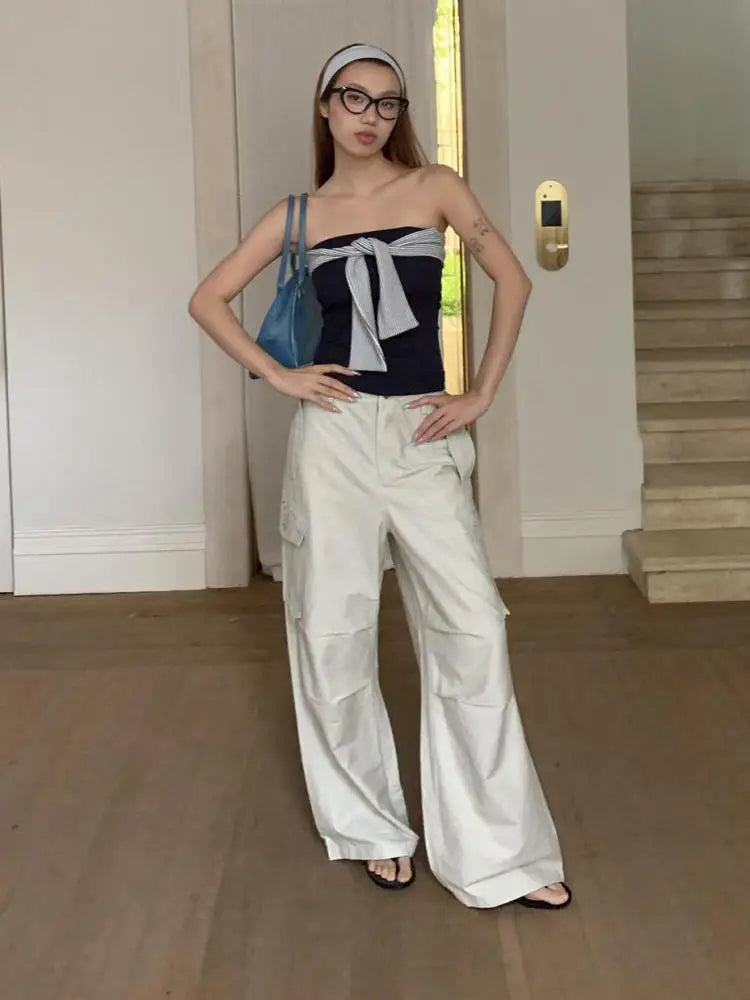 Woman in a stylish outfit with a black top and white pants, standing indoors.