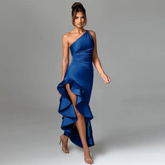 A satin long dress featuring a one shoulder design, ruffle accents, and an asymmetrical hem, shown on model.