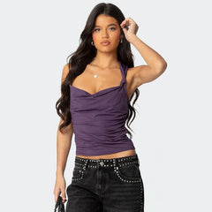 Woman wearing a purple halter top and black pants with studded details on a light gray background