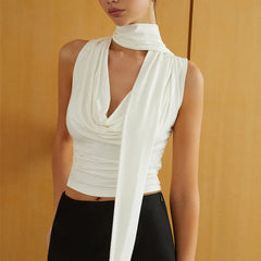 Woman wearing a white sleeveless top with a draped design against a mustard yellow background