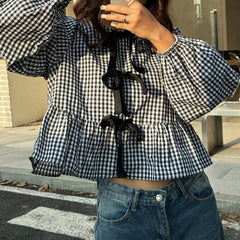 Person wearing a black and white checkered blouse with ruffled details and blue jeans.