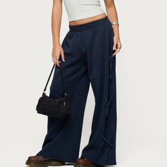 Person wearing navy wide-leg pants with lace-up sides, holding a black handbag on a light gray background.