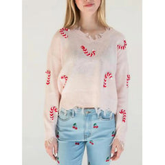 Person wearing a sheer pink sweater with red patterns and light blue jeans with cherry patterns.