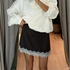 Person wearing a white oversized shirt and black lace-trimmed skirt indoors.