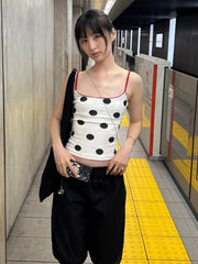 Woman in a polka dot top and black pants standing on a subway platform.