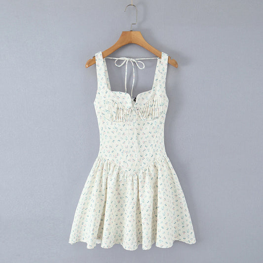 A sleeveless white mini dress with a small green and blue floral print, hanging on a wooden hanger against a solid gray background.