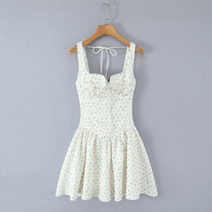 A sleeveless white mini dress with a small green and blue floral print, hanging on a wooden hanger against a solid gray background.
