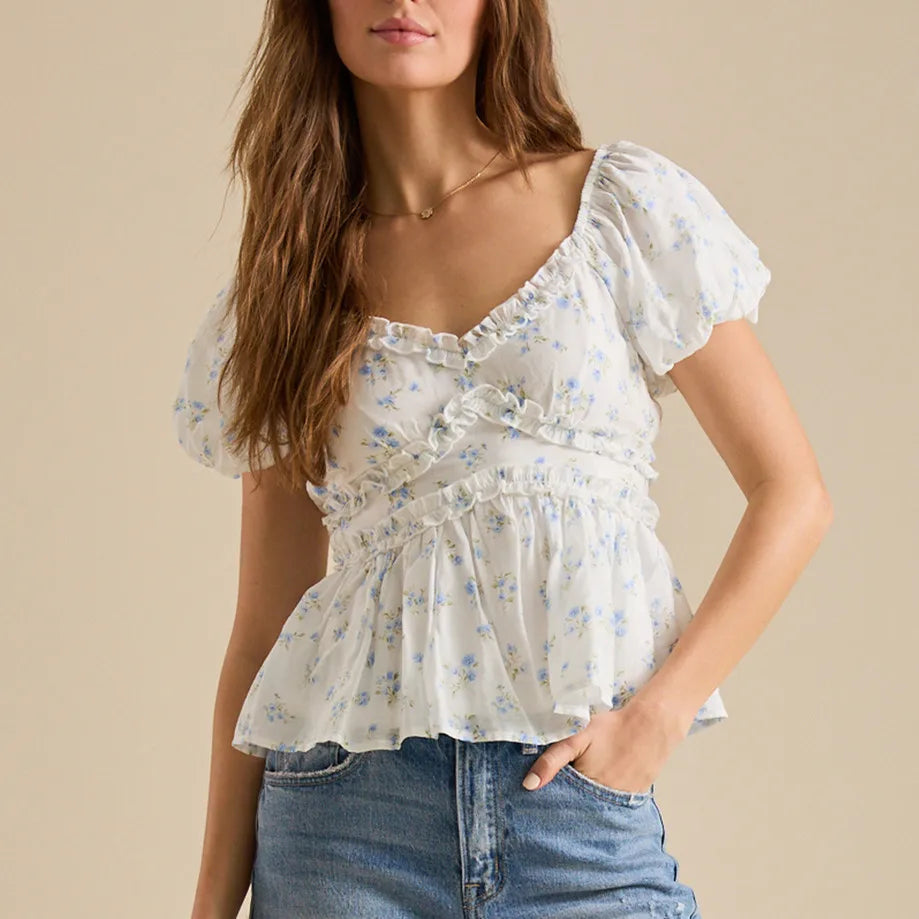 Woman wearing a floral blouse with ruffled details against a beige background