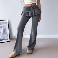 Person wearing gray ruffled pants and beige shoes in a minimalistic room.