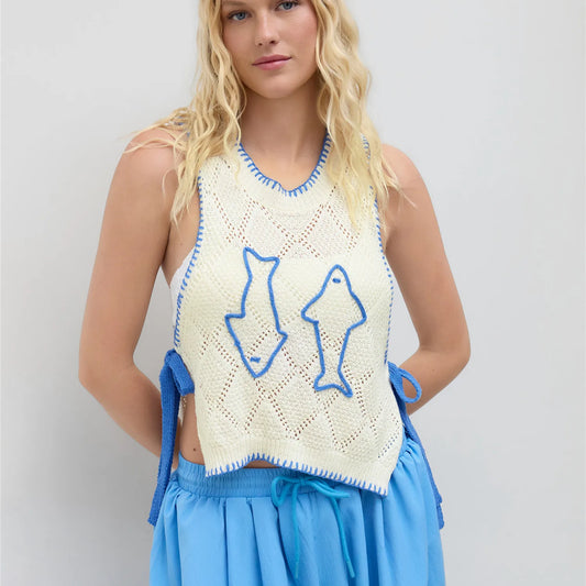 Woman wearing a crochet top with fish designs and blue shorts on a light gray background
