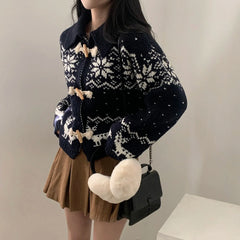 Person wearing a navy blue and white patterned cardigan with fluffy white pom-poms, holding a black handbag.