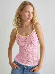 Woman wearing a pink lace tank top with yellow trim against a plain background