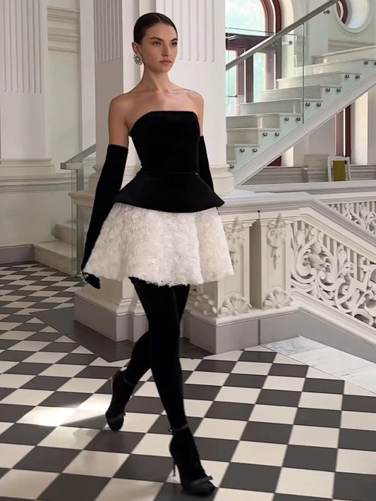 Woman in a black and white dress standing in an elegant interior setting with checkered floor and staircase.