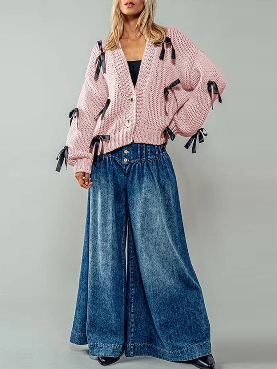 Person wearing a pink knitted cardigan with tassels and blue jeans 