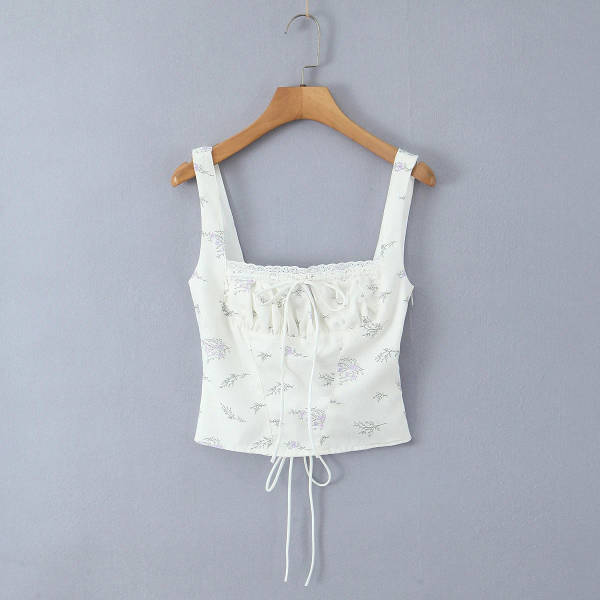 White lace crop top on a wooden hanger against a gray background