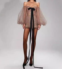 Woman wearing a sheer off-shoulder dress with a black bow and black stockings on a gray background