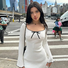 Woman in a white dress with a black bow standing on a city street.