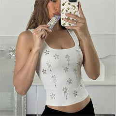 Woman taking a mirror selfie wearing a white tank top with floral patterns.