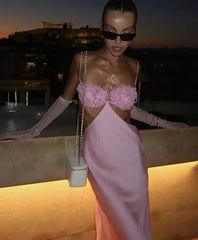 Woman in a pink dress with floral details standing on a rooftop at night.