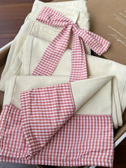 jeans with a pink gingham checkered ribbon on top, placed inside a cardboard box.