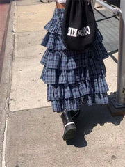 A woman wearing a blue plaid skirt with a layered ruffle hem, paired with a white top and boots for a chic fall look.