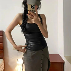 Person wearing a black tank top and gray skirt with a cap, taking a mirror selfie.