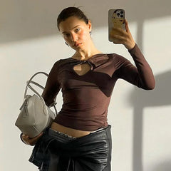 Woman taking a mirror selfie wearing a brown top and black leather skirt, holding a gray handbag.