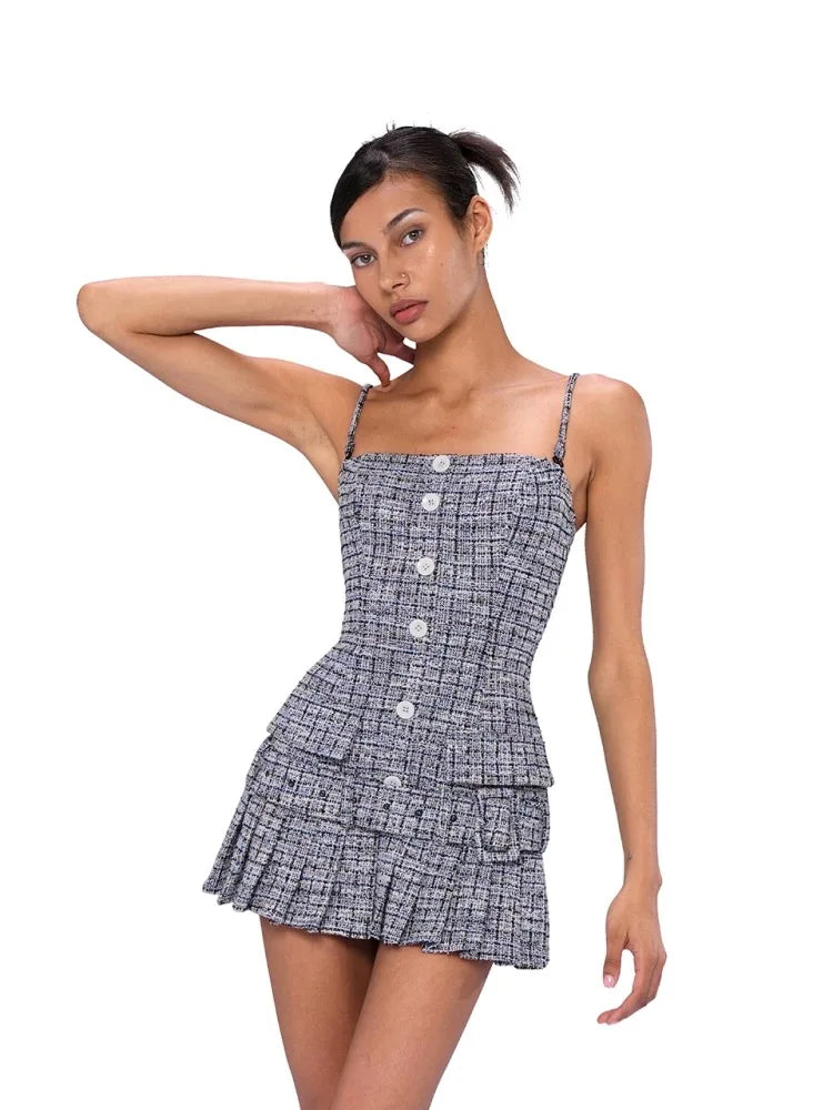 A woman modeling a sleeveless mini dress with a black and white micro-check pattern, featuring thin shoulder straps, a square neckline with decorative buttons, and a tiered ruffled skirt, set against a plain white background.
