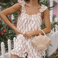 Woman wearing a floral dress holding a woven handbag outdoors.