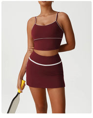 Woman wearing a maroon sports bra and skirt set holding a tennis racket 