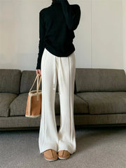 Person wearing a black sweater, white pants, and brown shoes in a living room.