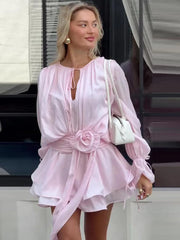Woman wearing a pink dress with a white handbag, standing in front of a building.