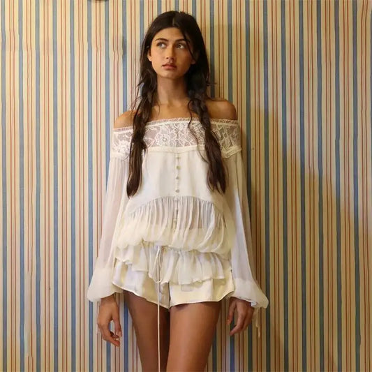 A woman modeling a white off-the-shoulder ruffled blouse and matching shorts set against a blue, beige, and white striped wallpaper background.