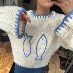 Person wearing a white sweater with blue fish designs and cuffs.