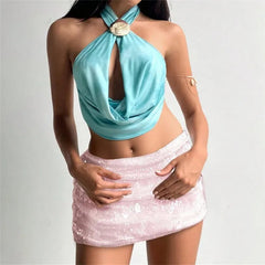 Woman wearing a turquoise halter top and white sequin skirt on a plain background
