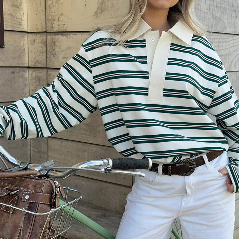 Person wearing a striped shirt and white pants standing next to a bicycle.