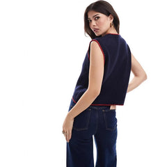Woman wearing a navy sleeveless top with red trim and dark jeans 