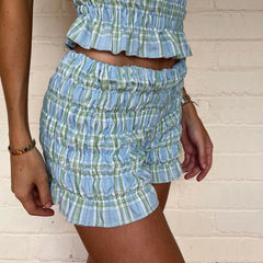 Person wearing a blue and green plaid outfit against a white brick wall.