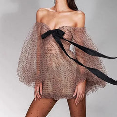 Woman wearing a sheer off-shoulder dress with a black ribbon on a gray background