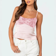 Woman wearing a pink lace top and white pants on a light gray background