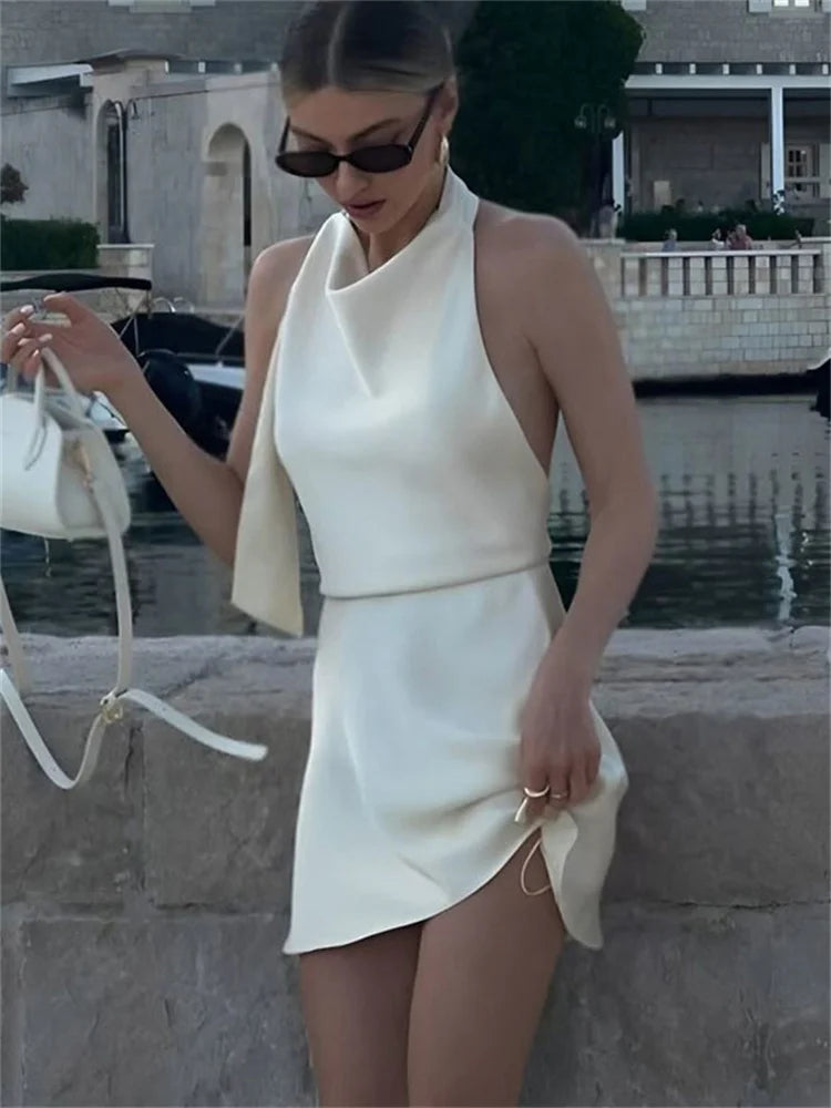 Woman in a white outfit standing by a waterfront with boats in the background