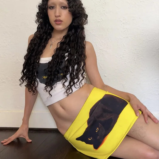 Woman holding a yellow towel with a black cat design against a white wall.