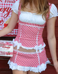 Person wearing a red and white checkered dress with lace details against a wooden background.