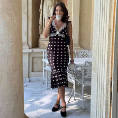 Woman in a black and white polka dot dress drinking from a teacup in an elegant outdoor setting.