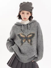 Person wearing a gray sweater with a butterfly design 