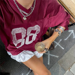 Person wearing a maroon sweatshirt with '88' design, white shorts, and holding a drink on a sidewalk.