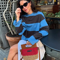 Woman wearing a blue and black striped sweater, sitting outdoors with a red and brown handbag.