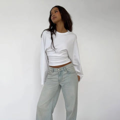 Person wearing a white long-sleeve top and light blue jeans against a plain background